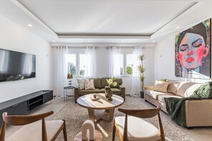 A modern living room with a flat-screen TV, a round coffee table, two sofas, and a large painting.