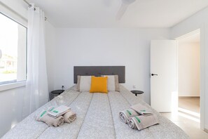 A bedroom with a bed, a headboard, two bedside tables, a window with curtains, and a door.