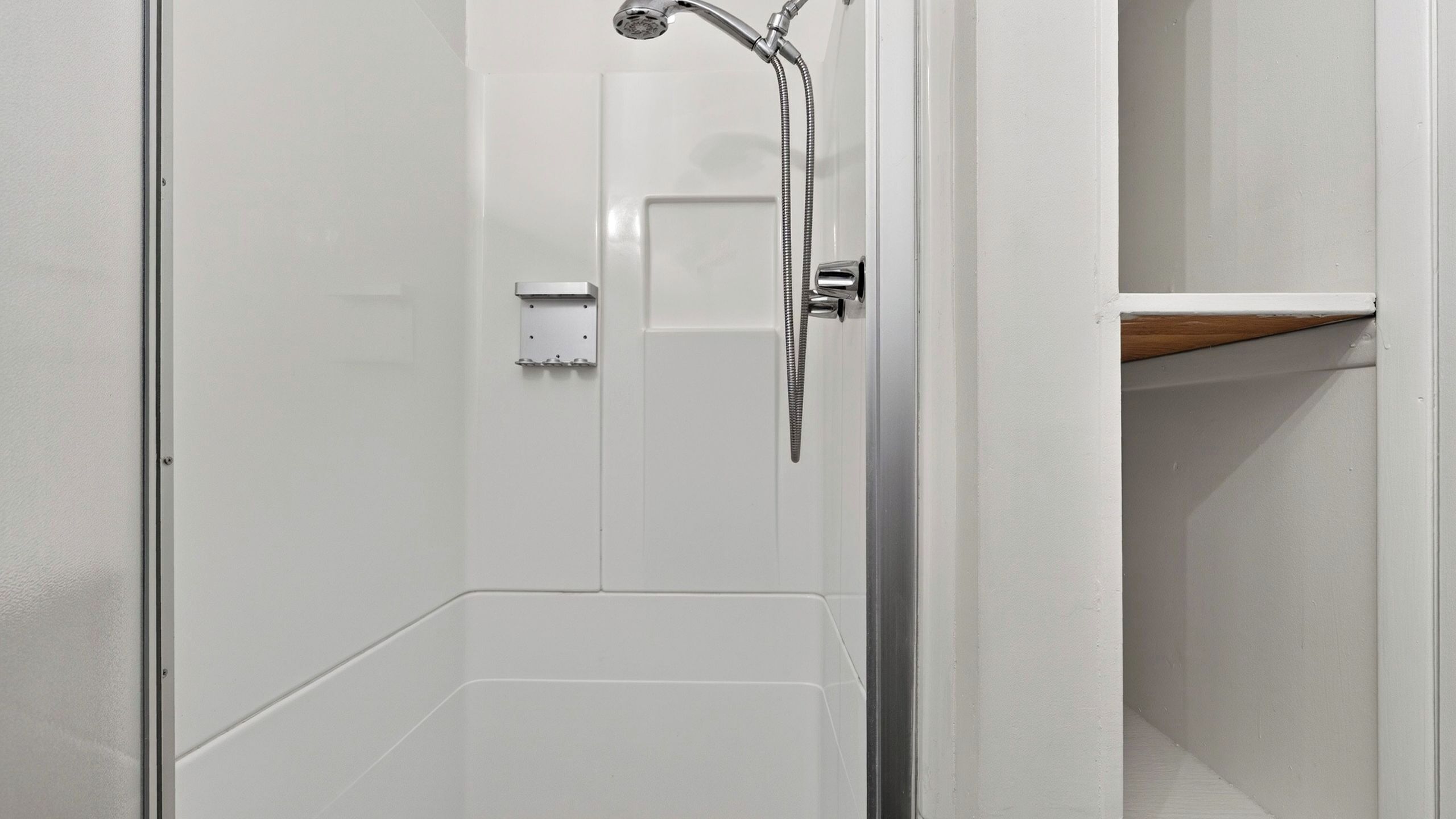Une salle de bain avec une douche, des toilettes et une étagère.