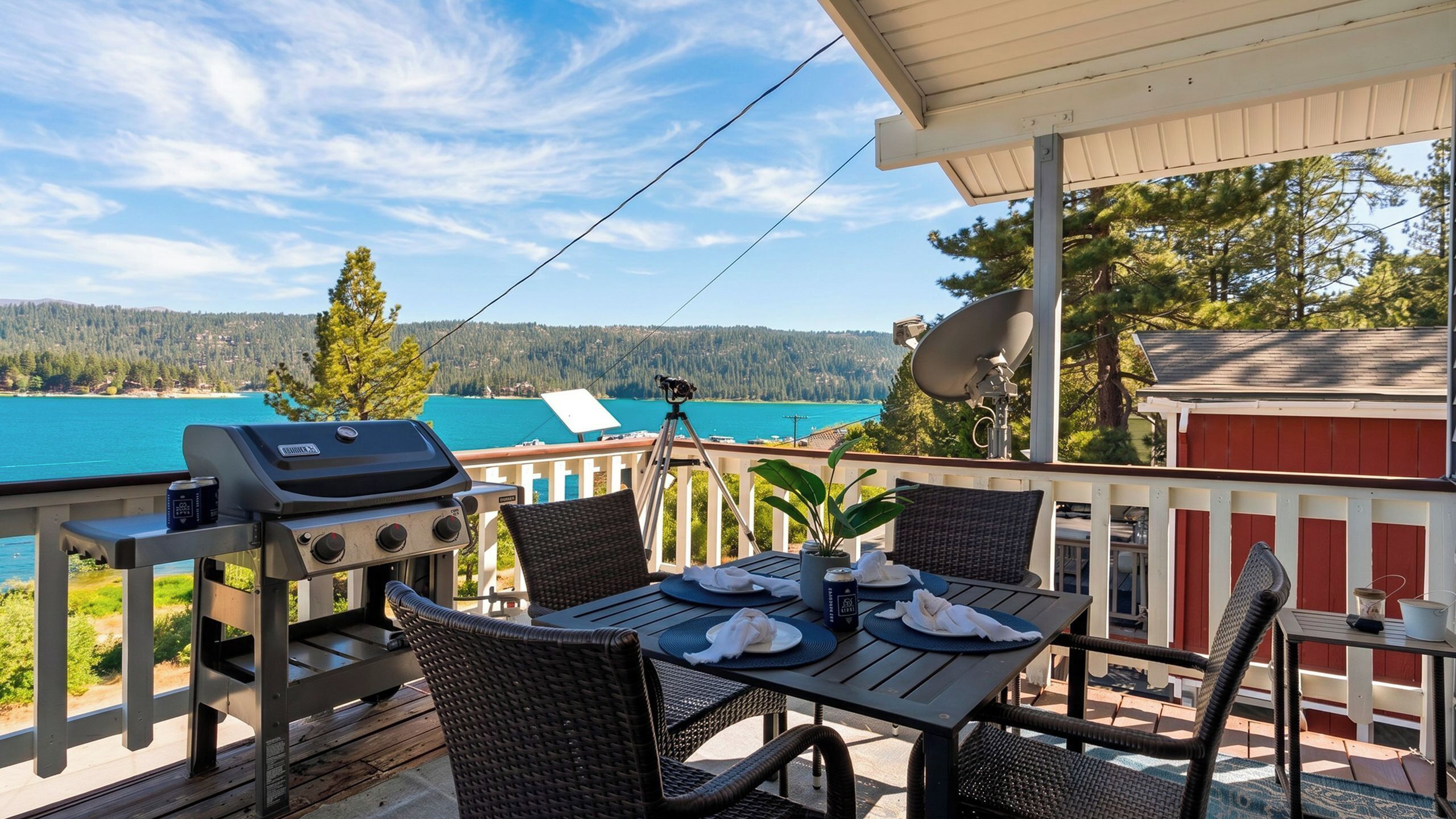 Una terraza con una parrilla, mesa de comedor, sillas y una vista panorámica de un lago y un bosque.