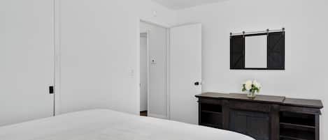 Ein Schlafzimmer mit Bett, Kommode, Spiegel und Tür.