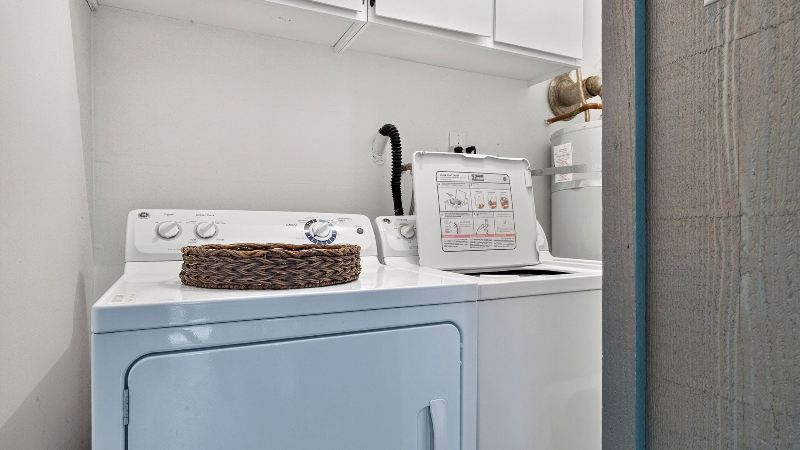 A laundry area with a washing machine, a dryer, and a wicker basket on the machine.