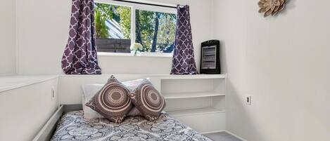 Un dormitorio con cama, ropa de cama estampada, una ventana con cortinas, un calentador y una decoración en la pared.