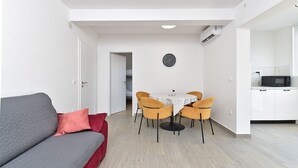 Un espacio habitable compacto con sofá, mesa de comedor, sillas, un reloj y una kitchenette.