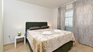 Un dormitorio ordenado con cama, mesita de noche, lámpara y cortinas.