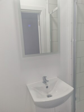 A bathroom with a white sink, a mirror, and a shower area. - City Centre, En-Suit double room-6, City View Place (Cambridge)