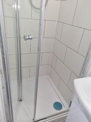 Un vestuario con mampara de vidrio, paredes de azulejos blancos y un objeto circular azul en el suelo.