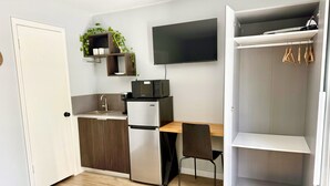 Eine kleine Küche mit Kühlschrank, Mikrowelle und Spüle, ein Holztisch, ein Stuhl und ein Kleiderschrank mit Kleiderstange.