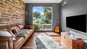 Ein modernes Wohnzimmer mit Steinwand, Ledersofa, großem Fenster, Gitarre und Flachbildfernseher.