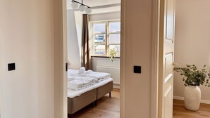 A bedroom with a bed, a window with curtains, a radiator, and a potted plant. - Heinason Collection - Old town & harbour (Thorshavn)