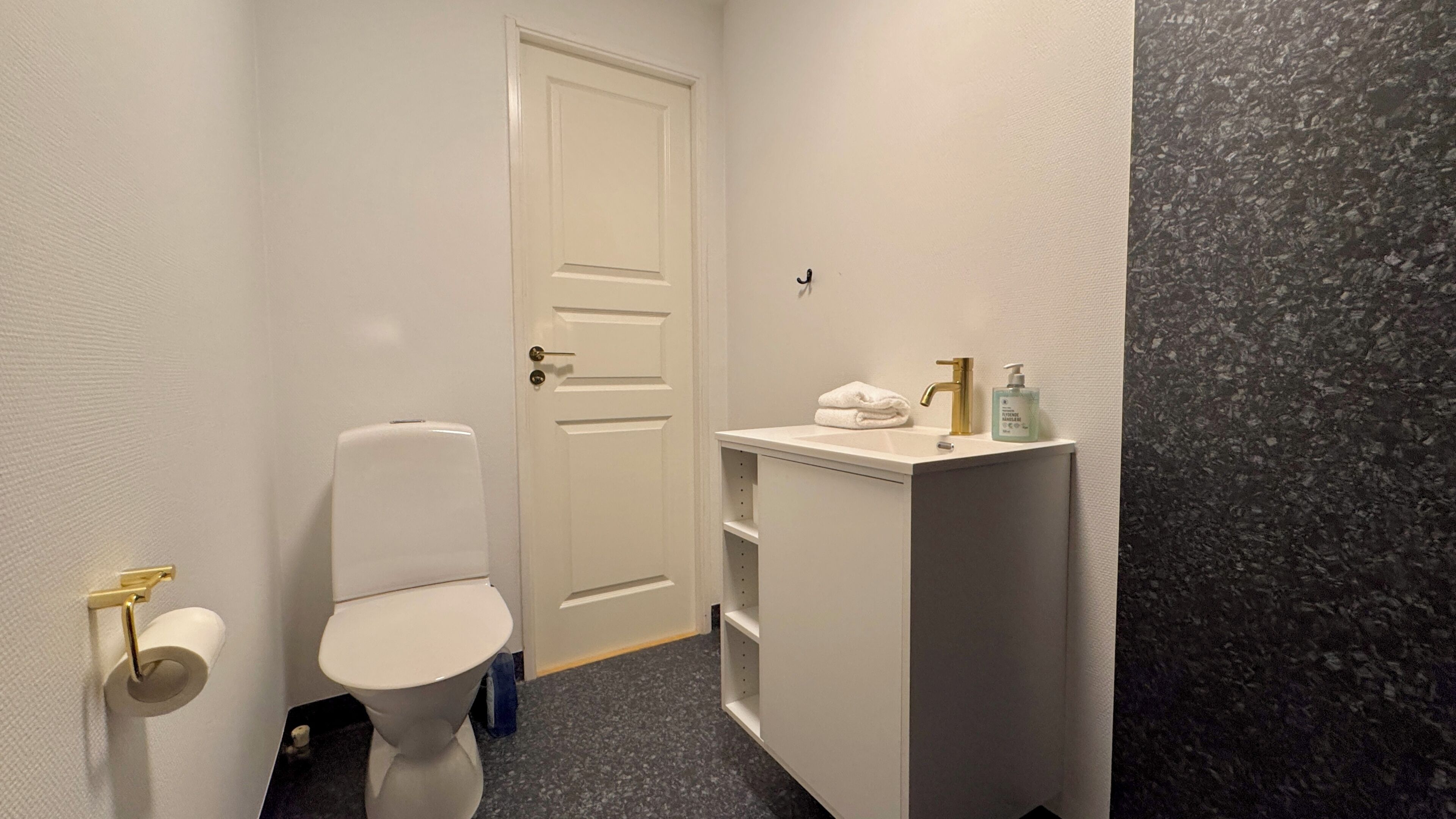 A small bathroom with a toilet, a sink with a towel, and a door.