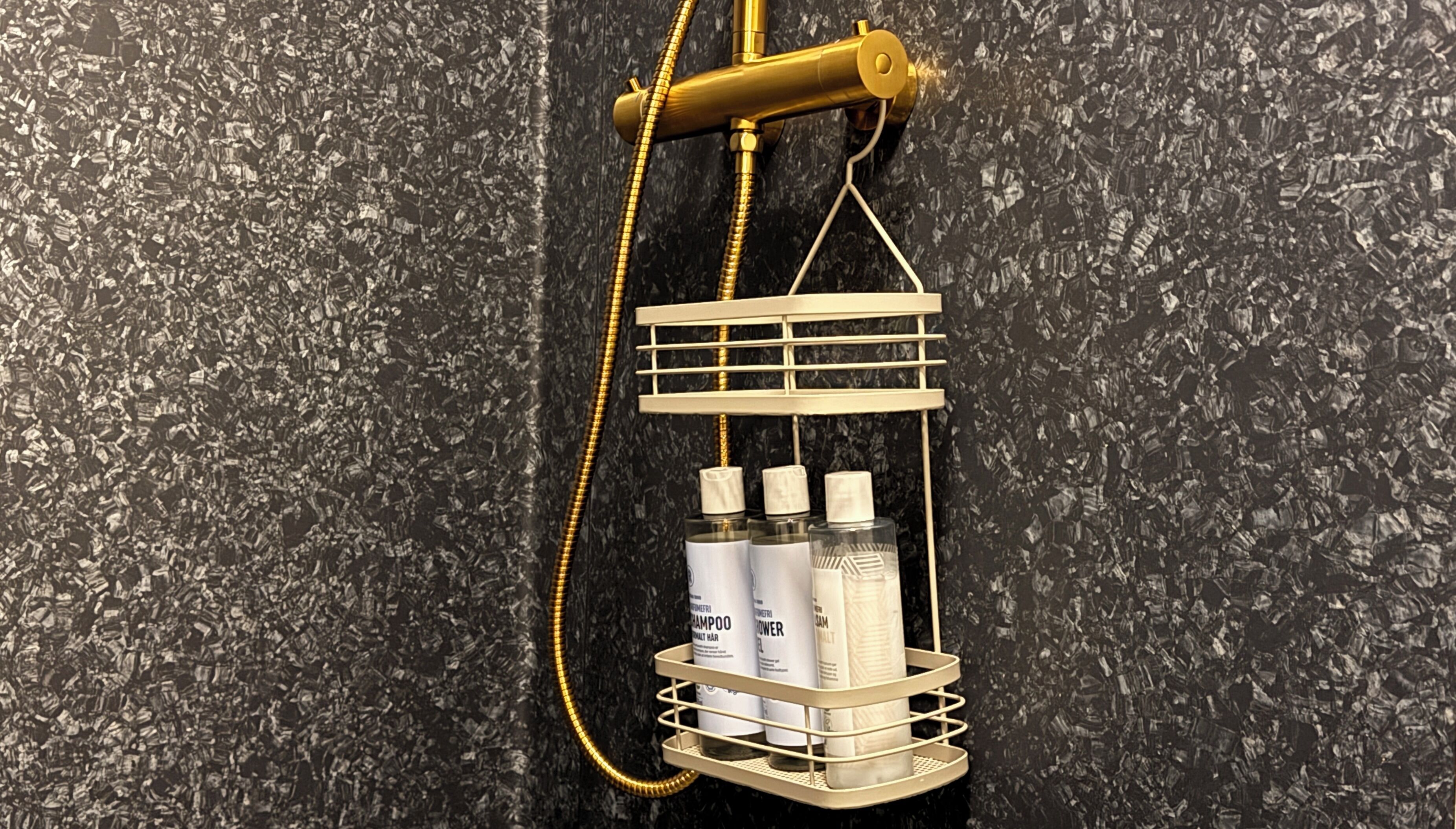 A shower with a gold showerhead and a white bottle holder with shampoo and conditioner.