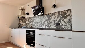 A modern kitchen with marble backsplash, built-in oven, and white cabinetry. - Heinason Collection - Old town & harbour (Thorshavn)