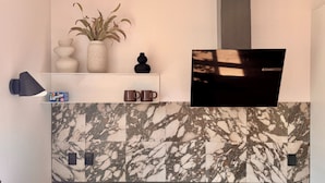 A modern kitchen with a marble backsplash, a white shelf with decorative items, and a black wall-mounted TV. - Heinason Collection - Old town & harbour (Thorshavn)