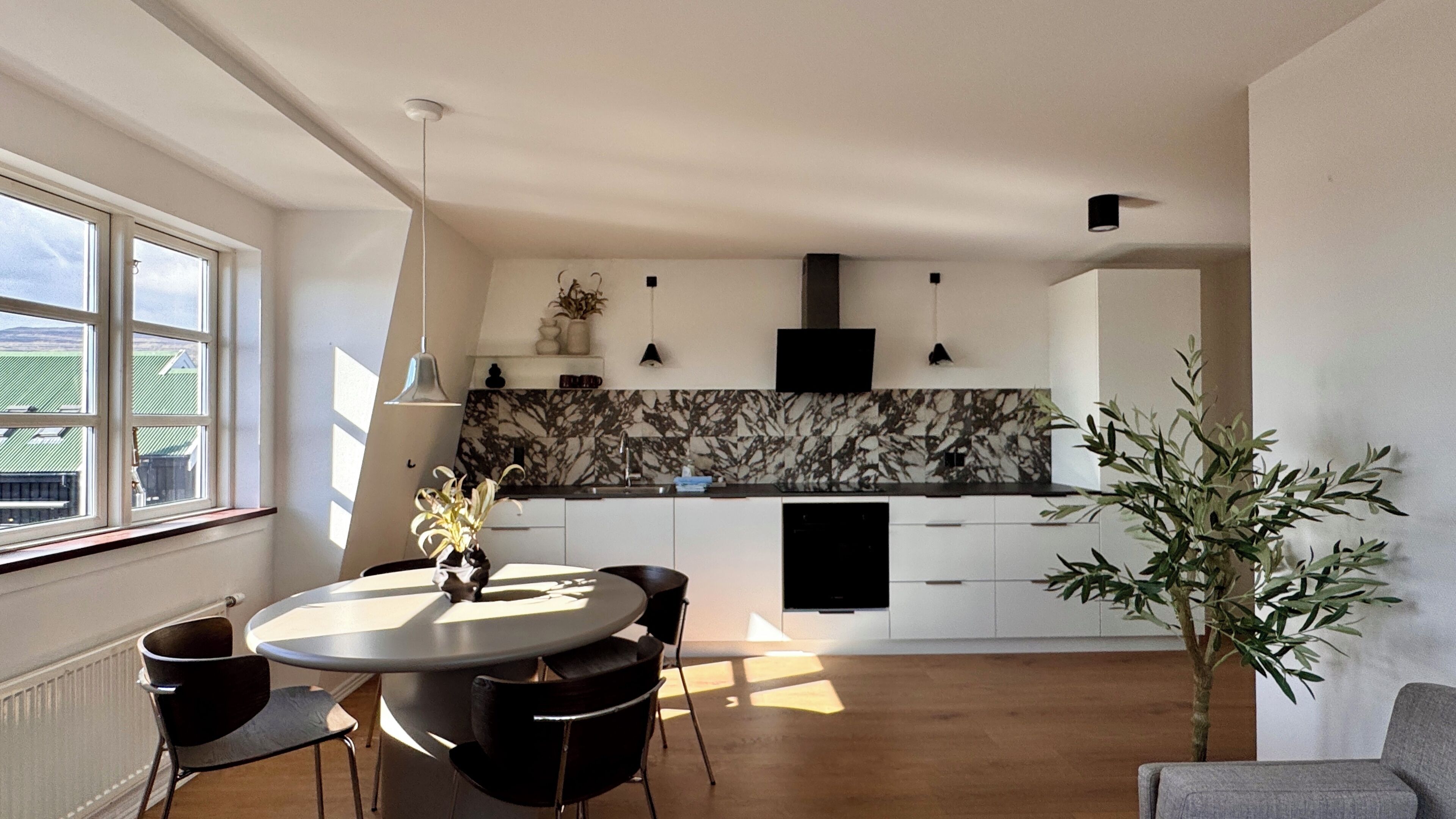 A modern kitchen with a marble backsplash, a dining area with a round table and chairs, and a large window providing natural light.