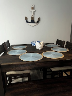 Ein Holztisch mit sechs Platzsets, einem weißen Dekorationsgegenstand und einer Wanddekoration in Form eines Ankers.
