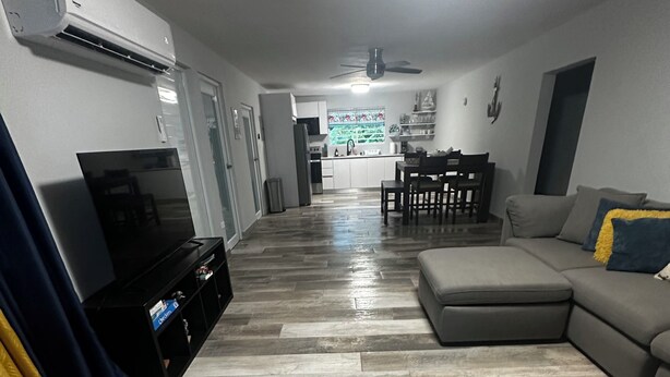A living room with a flat-screen TV, a sofa, a dining table, and a kitchen in the background. - Modern Tropical Oasis with Full Solar Power & AC – Minutes from Beaches! (Fajardo)