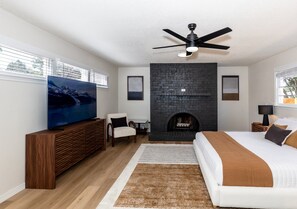Ein Schlafzimmer mit Bett, Fernseher, Kamin, Deckenventilator und Fenster.