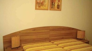 A bedroom with a wooden headboard, a bed with striped bedding, a bedside lamp, and two framed pictures on the wall. - Grand Resort Marina View Fort Beach (Nessebar)