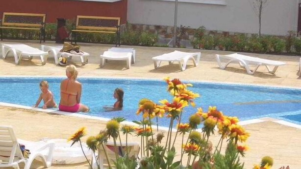 A swimming pool with lounge chairs, a building with windows, and a small tree. - Grand Resort Marina View Fort Beach (Nessebar)
