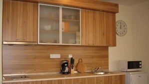 A kitchen with wooden cabinets, a microwave, a coffee maker, and a clock on the wall. - Grand Resort Marina View Fort Beach (Nessebar)