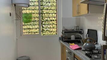 Cocina compacta con lavadora, estufa y ventana con vistas al verdor.