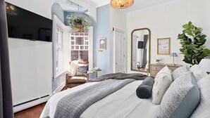 Ein Schlafzimmer mit Bett, Kommode, Spiegel, Pflanze und Fernseher.