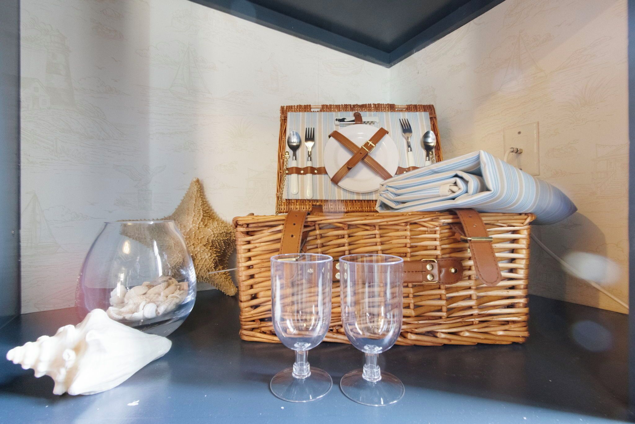 A wicker basket with cutlery and glasses, a starfish, and a glass bowl on a table.