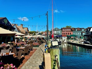 A waterfront dining area with outdoor seating, a dock with boats, and buildings with commercial establishments. - Luxury condo in the heart of Newport, walk everywhere (Newport)
