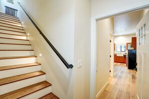 A staircase with wooden steps and a black handrail, leading to a kitchen area with wooden cabinets and a black refrigerator. - San Moritz Lake House | Walk to Lake Gregory | 3BR (Crestline)