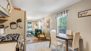 Cozinha com fogão, forno e armários, área de jantar com mesa e cadeiras, e sala de estar com sofá e janela.