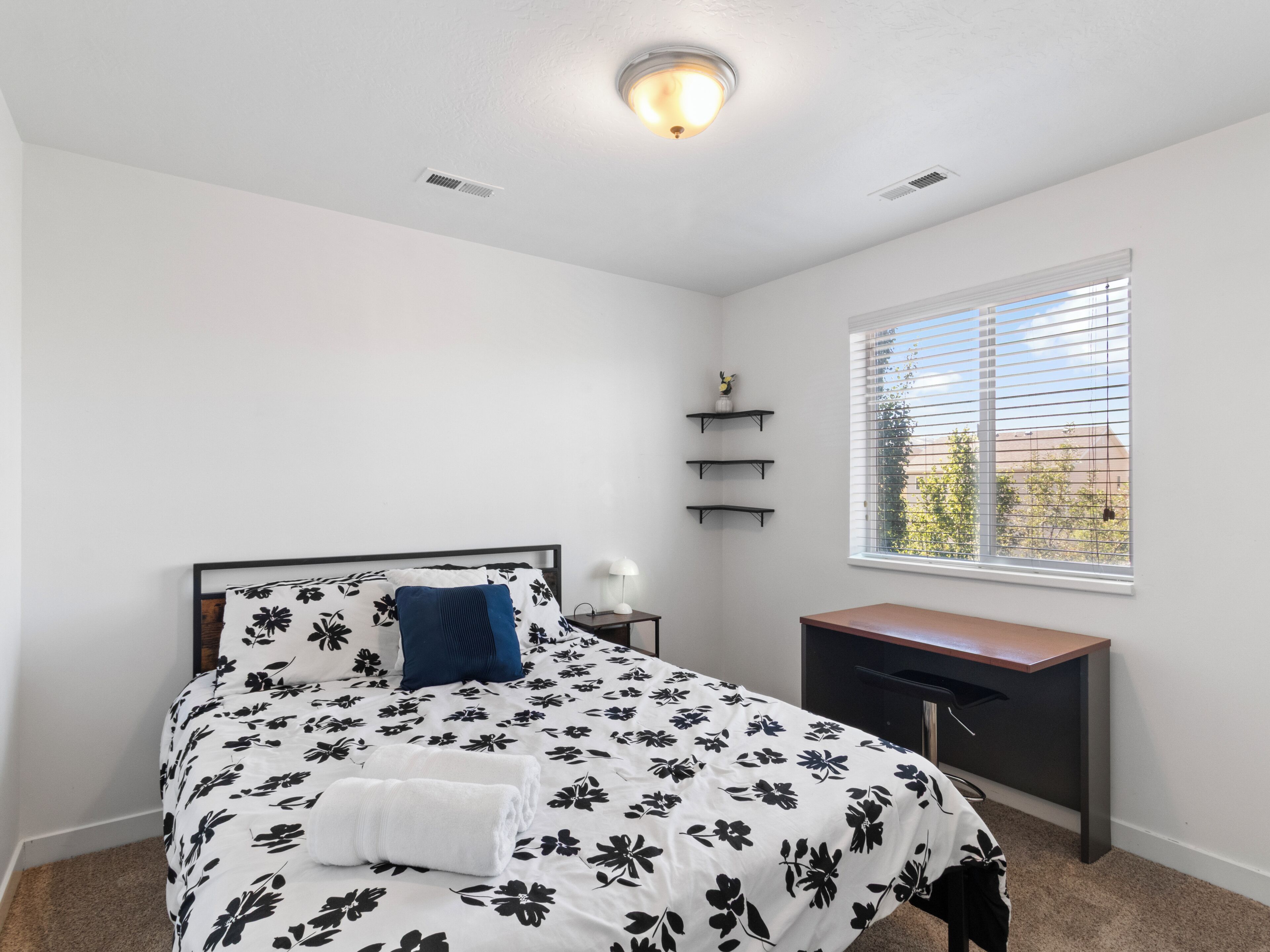 A bedroom with a bed, bedside table, lamp, window, and built-in shelves.