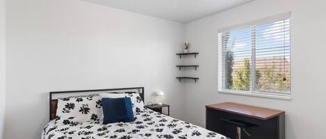 A bedroom with a bed, bedside table, lamp, window, and built-in shelves.