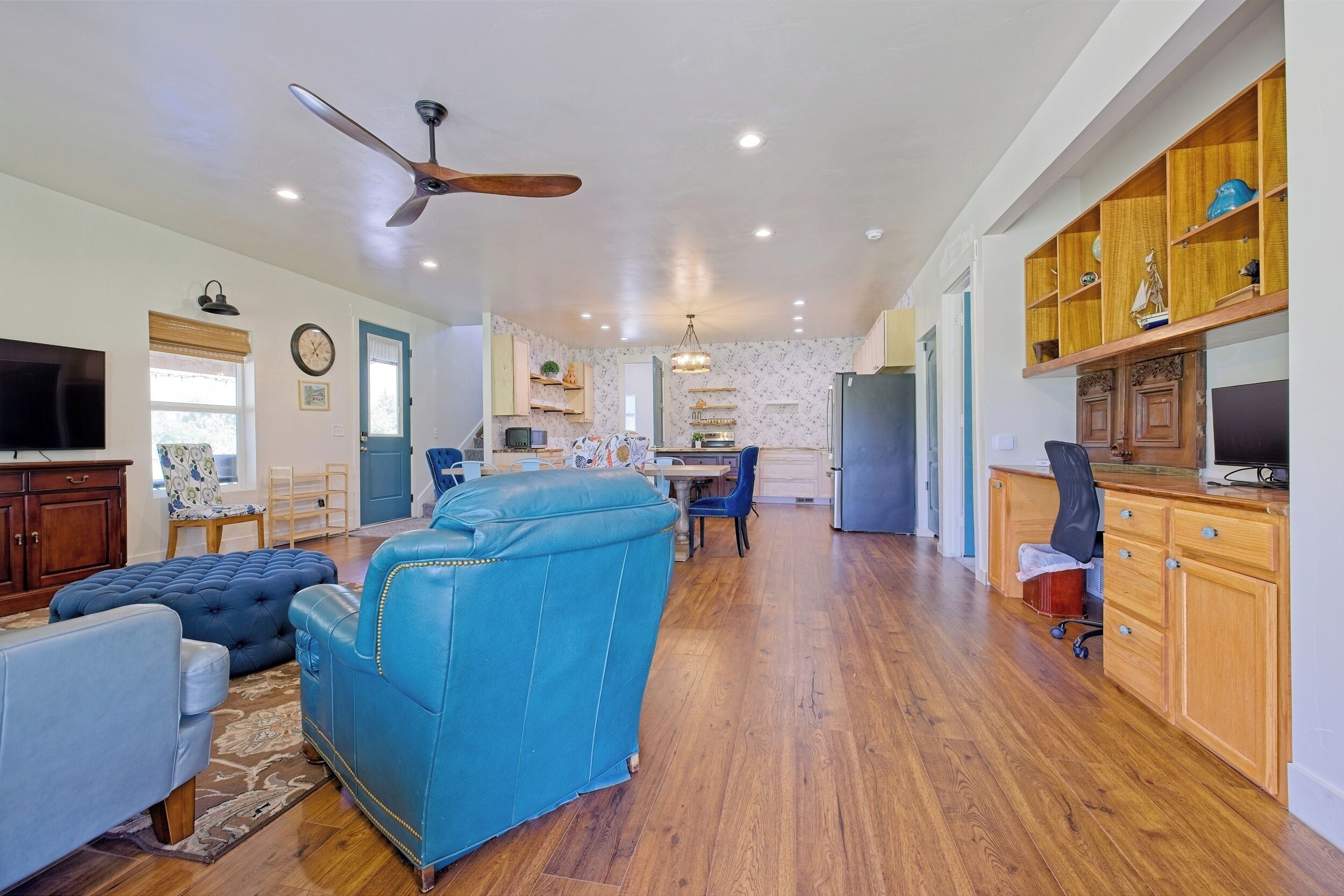 A spacious living area with a blue sofa, wooden cabinets, and a ceiling fan.
