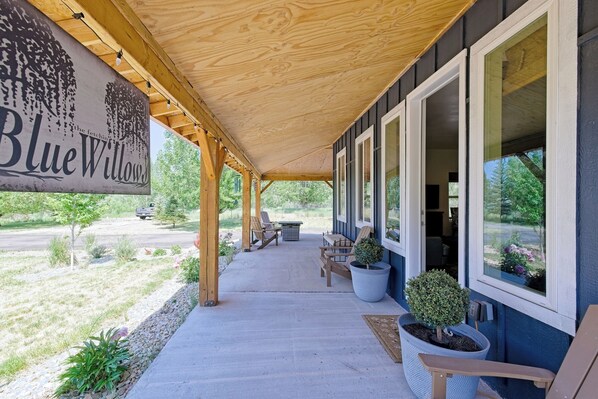 A covered porch with outdoor seating, a sign reading 'Blue Willow,' and a view of the surrounding landscape. - Blue Willows : Alpine Escape Home (Oakley)