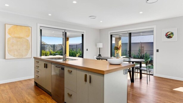 A modern kitchen with a central island, a dining area with a table and chairs, and a view of the outdoors. - Spacious Taupō Home - Arcade, Games, Walk to Lake (Taupō)