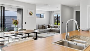 A modern kitchen with a central island, a dining area with a table and chairs, a built-in sofa, and a large window providing natural light. - Spacious Taupō Home - Arcade, Games, Walk to Lake (Taupō)