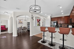 A modern kitchen with wooden cabinets, a stainless steel refrigerator, and a bar area with stools. - Universal Jurassic Family Fun Home | Home Theater (Little Elm)