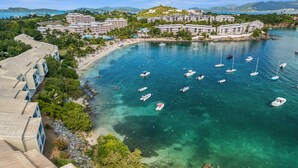 Un complex turístic costaner amb diversos edificis, una platja sorrenca i nombroses embarcacions a l'aigua.