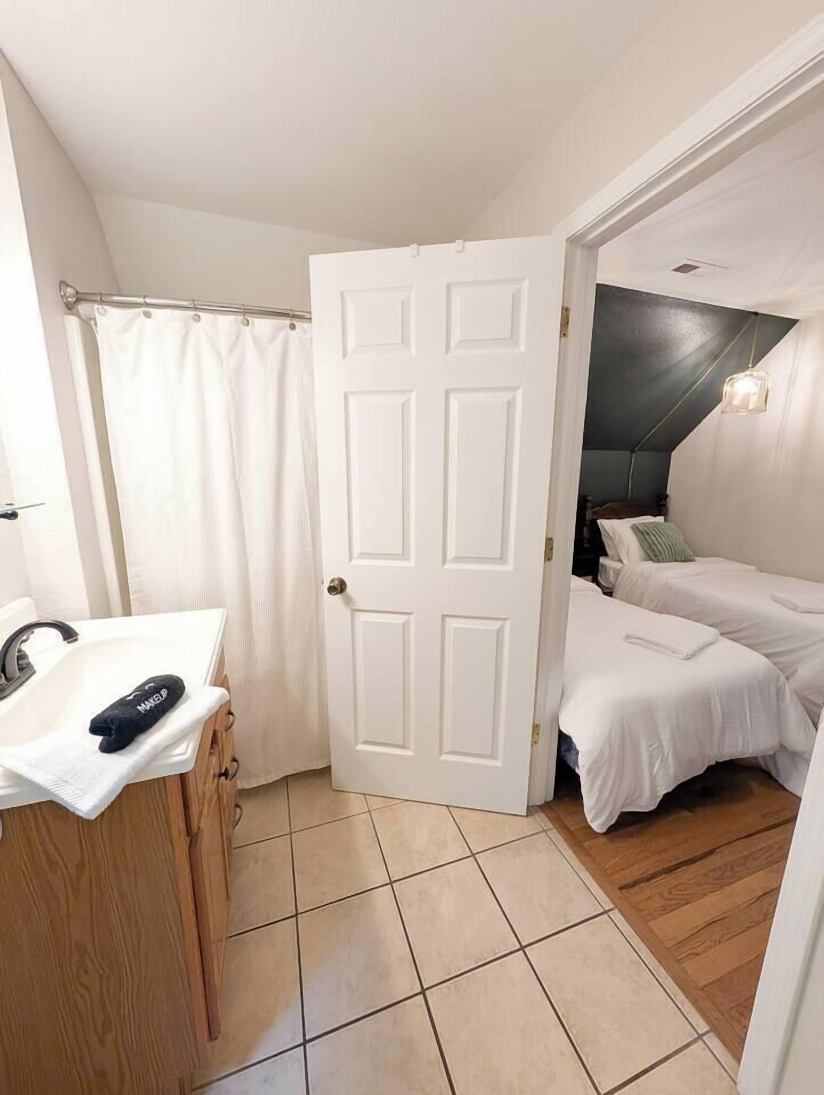 A small, clean room with a white door, a sink, and a bed with white bedding.