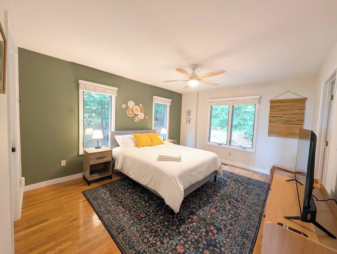 Quarto com cama, mesas de cabeceira, ventoinha no teto e um rack para TV.
