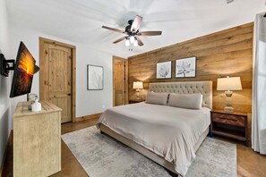 A bedroom with a bed, a ceiling fan, wooden paneling, and artwork on the walls. - Maison Bleue - Close to Downtown | Game Room | Firepit (Blue Ridge)