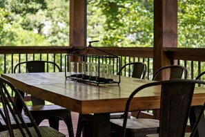 A wooden table with chairs, a candle holder, and a view of greenery through a wooden railing. - Maison Bleue - Close to Downtown | Game Room | Firepit (Blue Ridge)