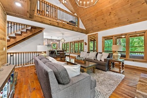 A spacious living area with a high ceiling, wooden staircase, and large windows offering a view of the outdoors. - Maison Bleue - Close to Downtown | Game Room | Firepit (Blue Ridge)