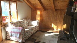 Un'accogliente stanza con un divano a motivi floreali, un soffitto in legno e una finestra con tende.