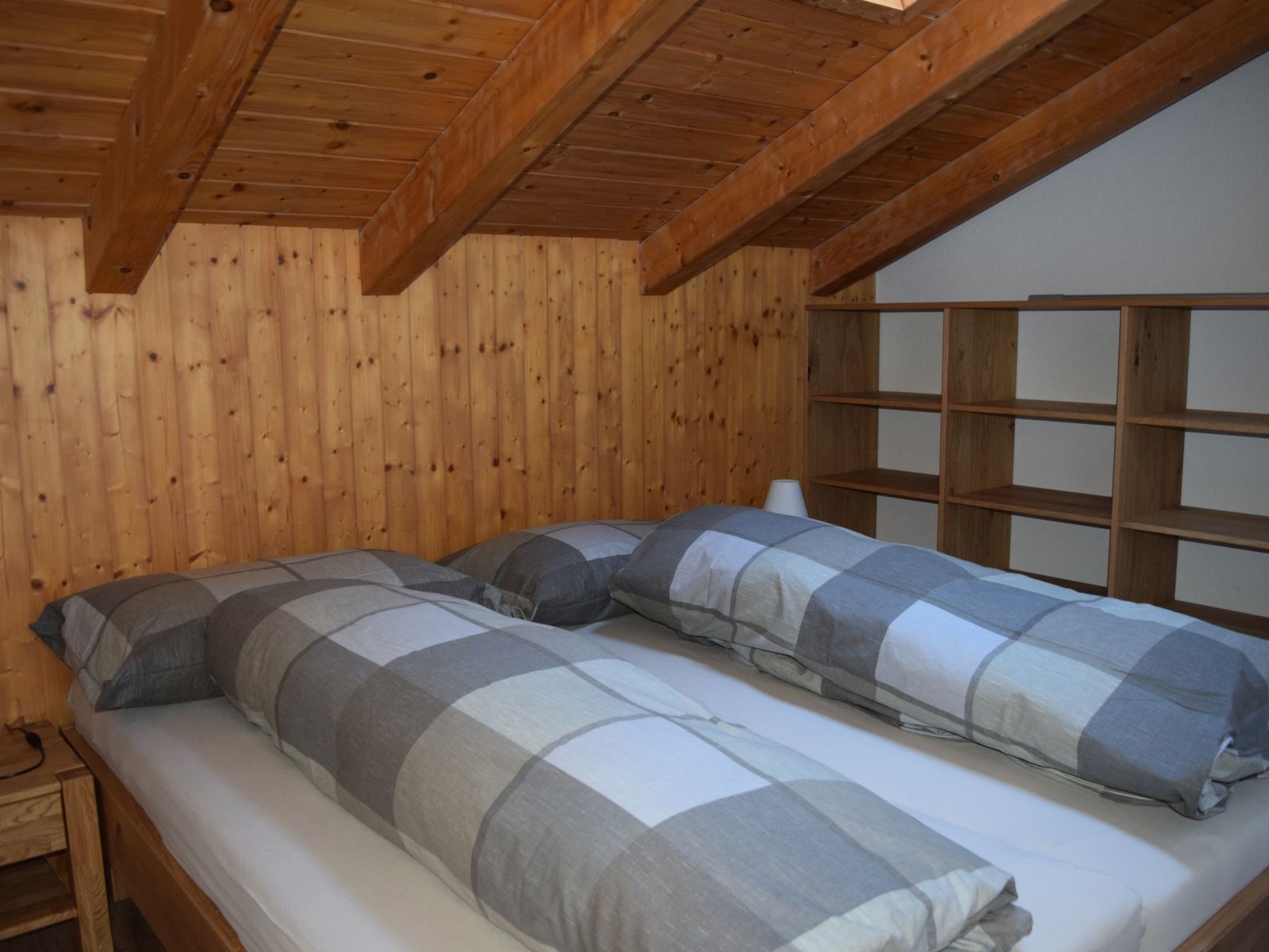 A wooden cabin room with two beds, a wooden shelf unit, and a window.