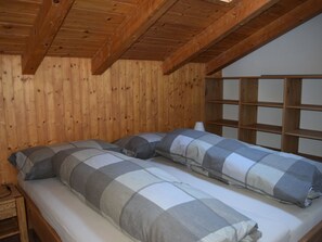 Una habitación de cabaña de madera con dos camas, una estantería de madera y una ventana.
