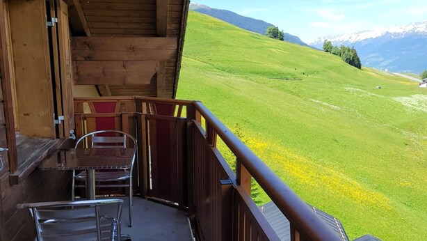 Una baita di legno con un balcone che si affaccia su una valle verde e montagne.