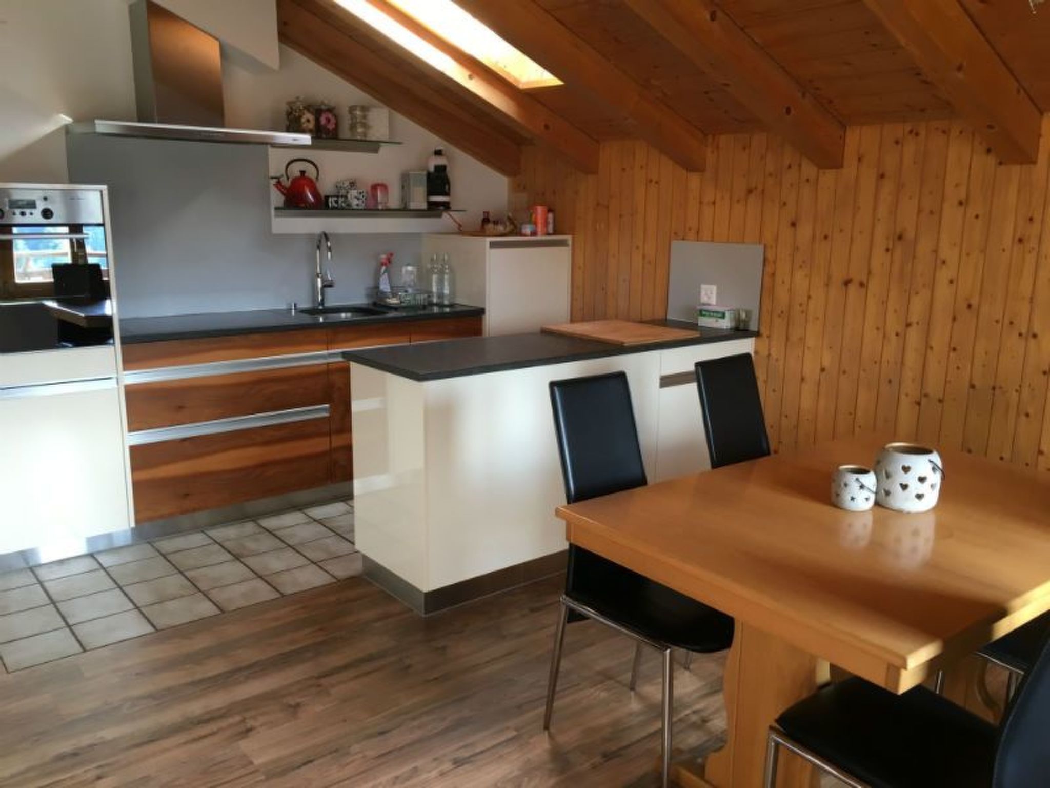 Ett modernt kök med vita köksskåp, ett matbord i trä och svarta stolar.