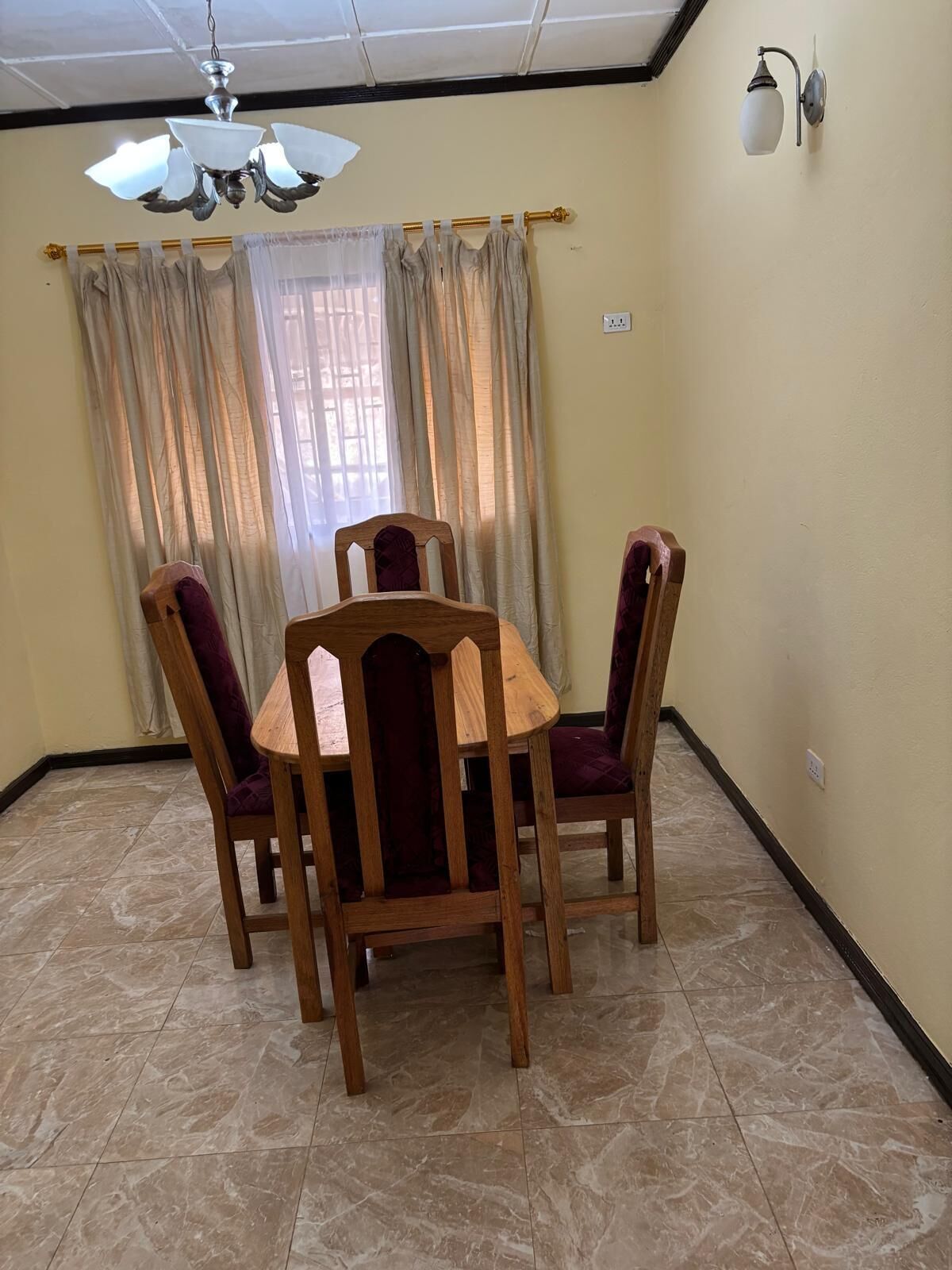 Un comedor con una mesa y sillas de madera, un ventilador de techo y una ventana con cortinas.